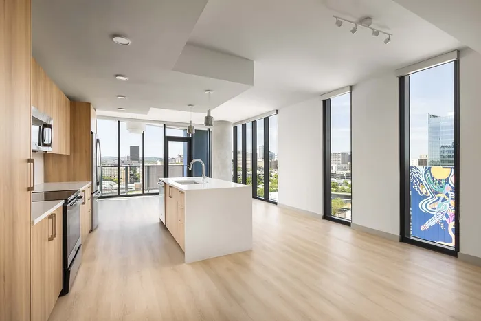 Modern open-concept kitchen in a bright apartment with panoramic city views, featuring sleek wood cabinetry and a spacious island.