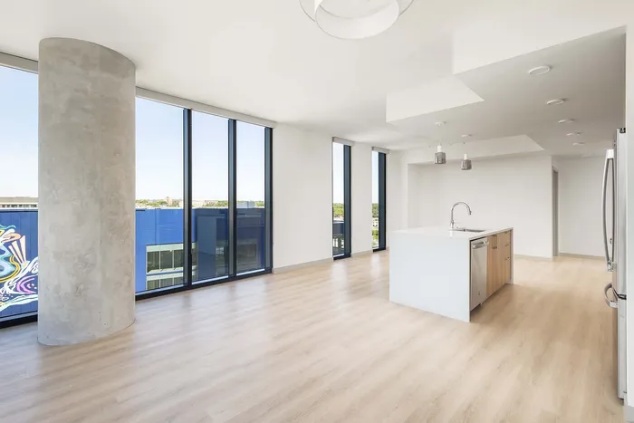 Bright, modern apartment interior with floor-to-ceiling windows offering stunning city views, sleek wooden floors, and a stylish kitchen island.