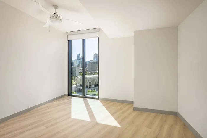 Bright, modern apartment room with sleek wooden floors and floor-to-ceiling windows offering stunning city views.