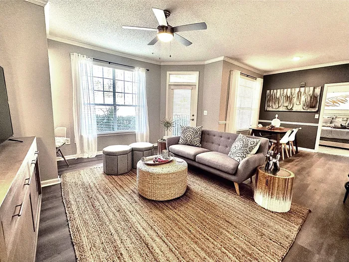 Bright, modern living room with stylish decor, featuring a cozy gray sofa, woven coffee table, and elegant dining area, perfect for relaxing and entertaining in a chic apartment setting.