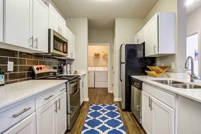 Modern kitchen with sleek stainless steel appliances, white cabinetry, and a charming blue patterned runner.