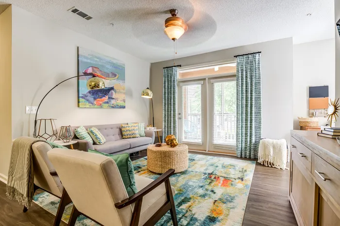 Inviting living room with chic decor, featuring a cozy gray sofa, colorful rug, and modern art on the wall, bathed in natural light from large windows.