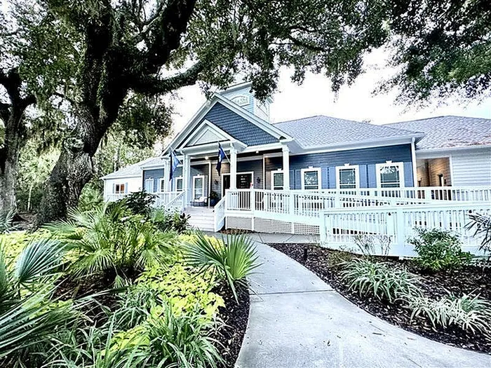 Charming blue and white cottage-style house with a welcoming porch, nestled among lush greenery and mature trees.