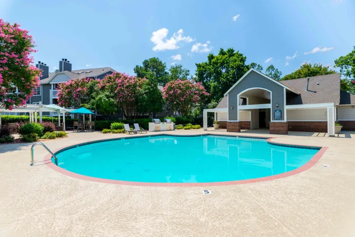 \Inviting outdoor swimming pool surrounded by lush greenery and colorful floral landscaping, with charming clubhouse nearby.