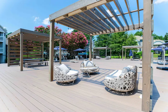 Charming outdoor deck with elegant wicker chairs and modern pergolas, offering a relaxing space under a clear blue sky, surrounded by lush greenery.