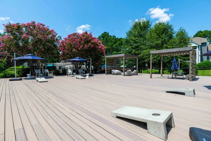 Expansive wooden deck with modern lounge chairs, elegant pergolas, and lush pink blossom trees in a serene garden setting.