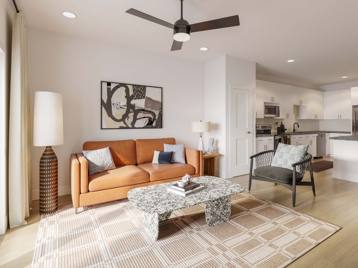 Chic living room with a modern leather sofa, abstract artwork, and an open kitchen design, accentuated by a stylish ceiling fan.