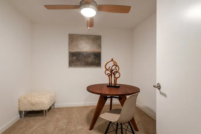 Inviting home office space with chic round table, contemporary art piece, and plush seating, enhanced by a stylish ceiling fan.