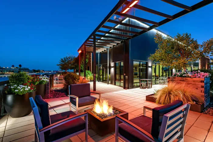 Chic rooftop patio at twilight with modern seating around a cozy fire pit, lush planters, and stylish lighting on a contemporary building.