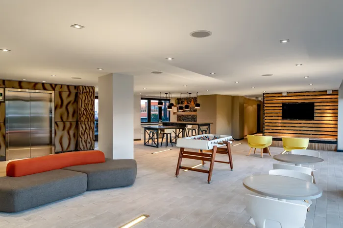 Modern apartment lounge featuring chic decor, bright lighting, a foosball table, stylish seating, and a cozy dining area with pendant lights.
