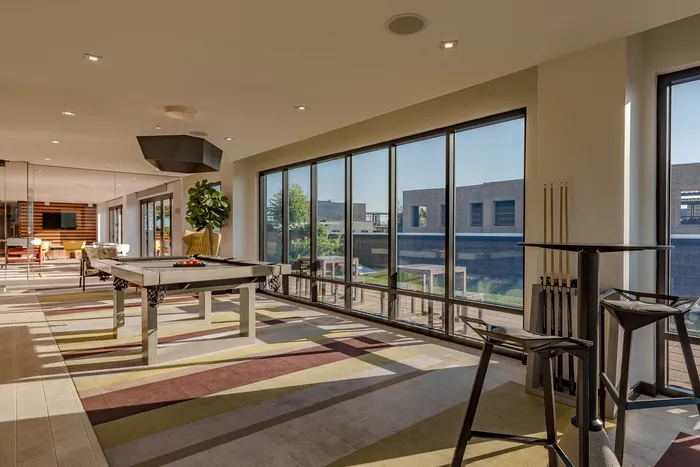 Elegant recreation room with a modern pool table, large windows offering ample natural light, and stylish furnishings.