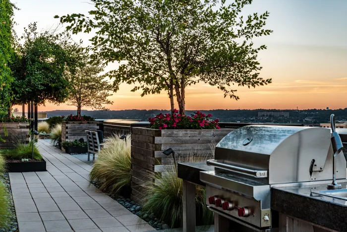 Chic rooftop patio with modern grill, lush greenery, and stunning sunset views.