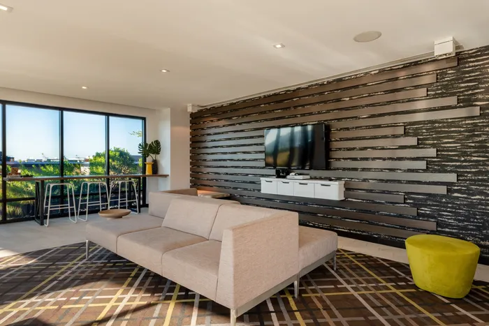 Modern living room with sleek decor, featuring a beige sofa, stylish striped accent wall with mounted TV, and large windows offering a scenic view.
