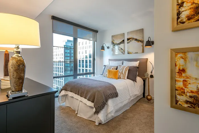Chic urban bedroom with floor-to-ceiling windows, elegant decor, and plush textiles, offering a cozy and modern living space.