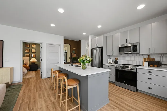 Modern kitchen with sleek gray cabinets, stainless steel appliances, and a large white island with bar seating and a vase of fresh flowers.