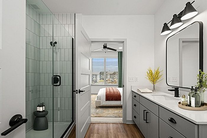 Modern bathroom featuring a sleek vanity, elegant glass shower, and view of a well-lit bedroom with large windows.