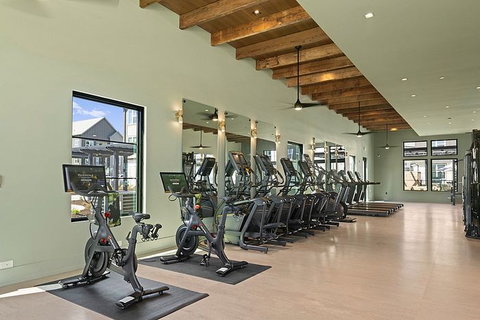 Modern fitness center with state-of-the-art equipment, sleek design, and large windows offering natural light.