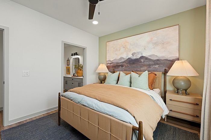 Cozy bedroom oasis with a plush bed, elegant bedside lamps, and serene mountain artwork on mint green accent wall.
