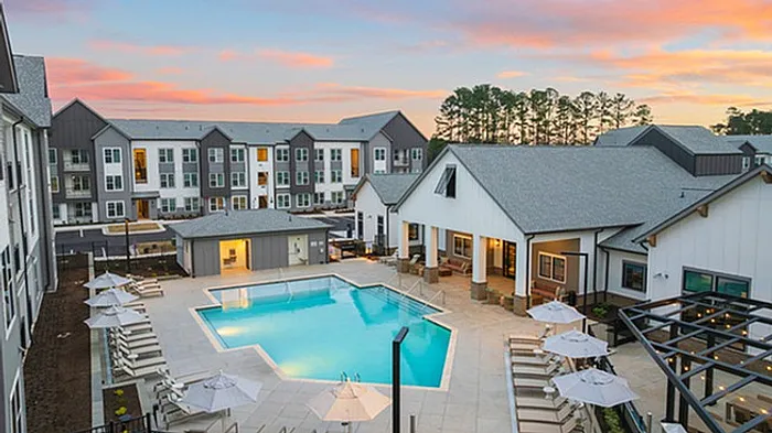 Charming apartment complex featuring a sparkling outdoor pool surrounded by modern architecture and inviting lounge areas at sunset.