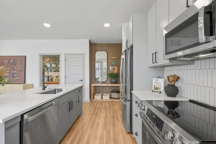 Modern kitchen with sleek grey cabinetry, stainless steel appliances, and elegant wood flooring, leading into a stylishly decorated living space.
