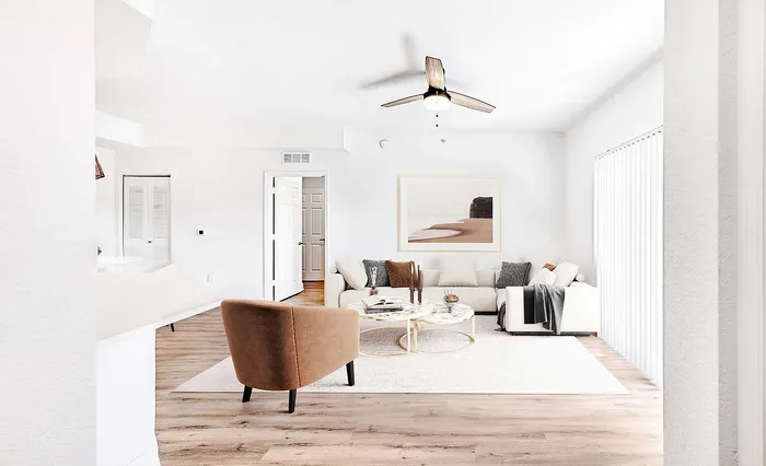 Bright and modern living room with elegant decor, featuring a cozy white sofa, sleek wooden flooring, and a stylish ceiling fan.