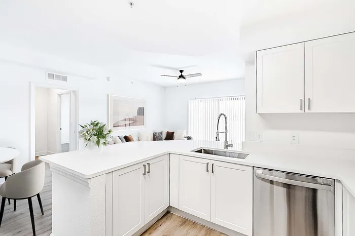 Bright, airy kitchen with sleek white cabinetry, modern fixtures, and open layout leading to a cozy living area.
