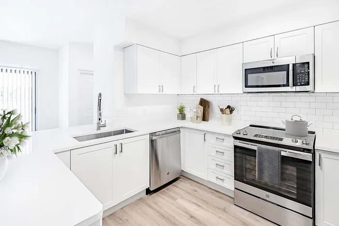 Bright, modern kitchen with sleek white cabinetry, stainless steel appliances, and elegant wood flooring.