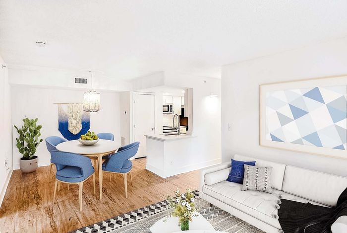 Modern apartment interior showcasing an open-concept dining and living area with chic blue chairs, cozy white sofa, and stylish kitchen access.