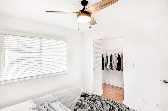 Bright and airy bedroom with modern ceiling fan, large window, and adjoining walk-in closet.