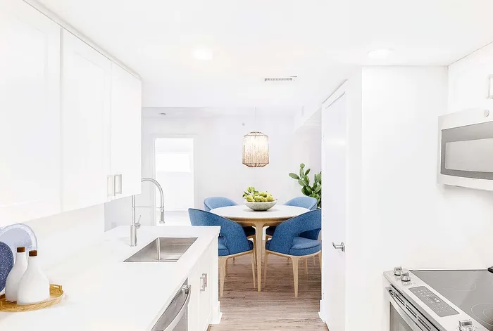 Bright, contemporary kitchen with sleek white cabinetry and stylish dining area featuring blue chairs and a modern light fixture.