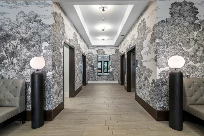 Elegant hallway with sophisticated black and white tree-patterned wallpaper, modern lighting, and sleek elevators.