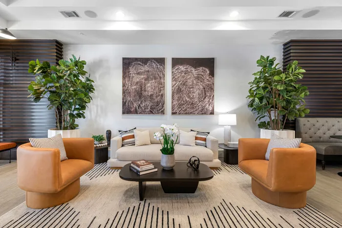 Sophisticated living room featuring plush beige sofa, stylish leather chairs, modern art, and lush greenery for an elegant ambiance.