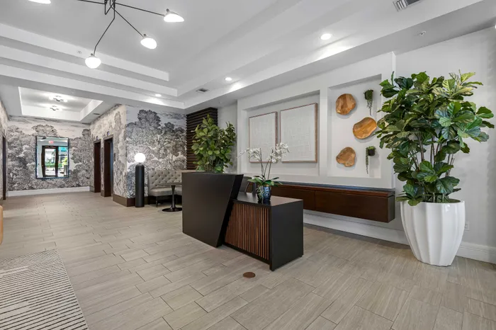Elegant apartment lobby with modern decor, featuring stylish lighting, lush greenery, and sophisticated wall art.