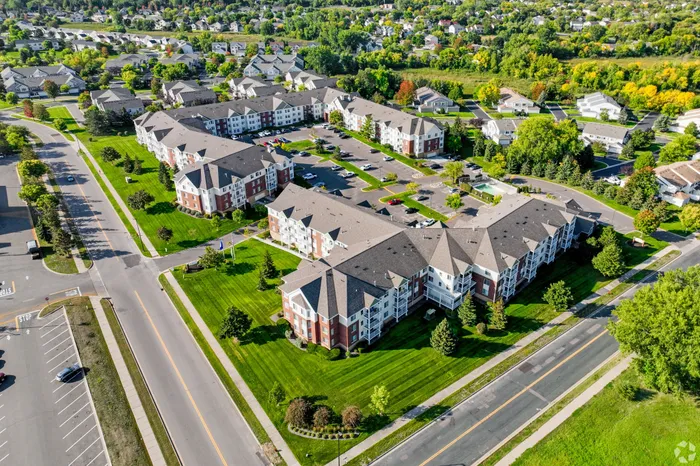 Aerial view of a charming suburban apartment community with lush green landscaping, spacious parking, and picturesque neighborhood surroundings.