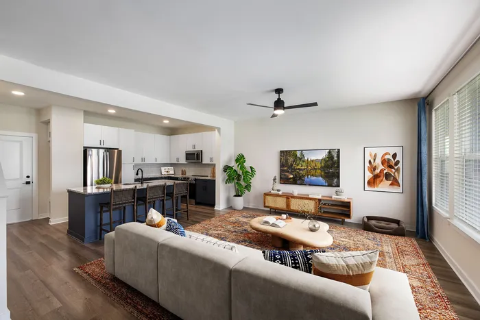 Modern open-concept living space featuring a cozy sofa, stylish decor, and a spacious kitchen with sleek appliances and kitchen island..