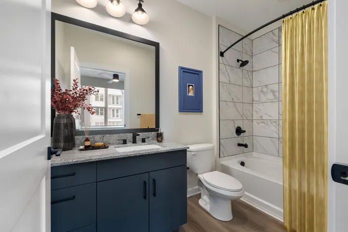 Elegant bathroom featuring a sleek granite countertop, navy blue vanity, modern lighting, and a stylish shower with tiled surrounds.