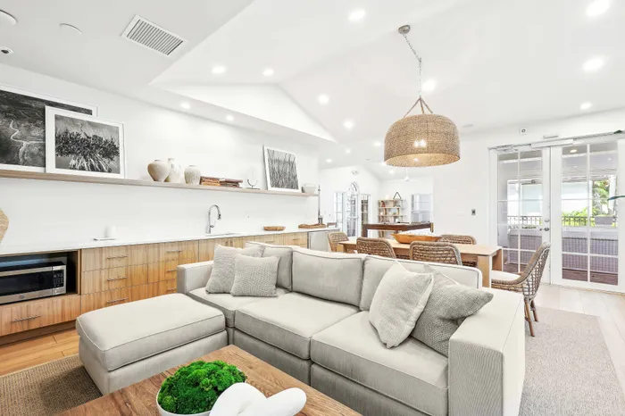 Bright and airy open-concept living room and dining area featuring elegant decor, a cozy sectional sofa, and a stylish woven pendant light.