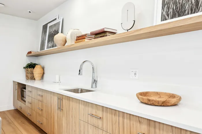 Modern kitchen with sleek wood cabinets, elegant floating shelf with decorative jars and books, and minimalist design elements.