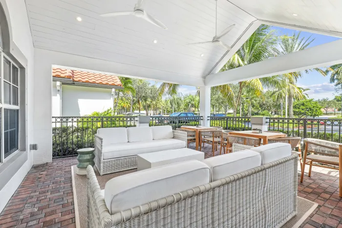 Charming outdoor patio with elegant wicker seating, wooden dining tables, and lush palm views under a stylish covered ceiling.