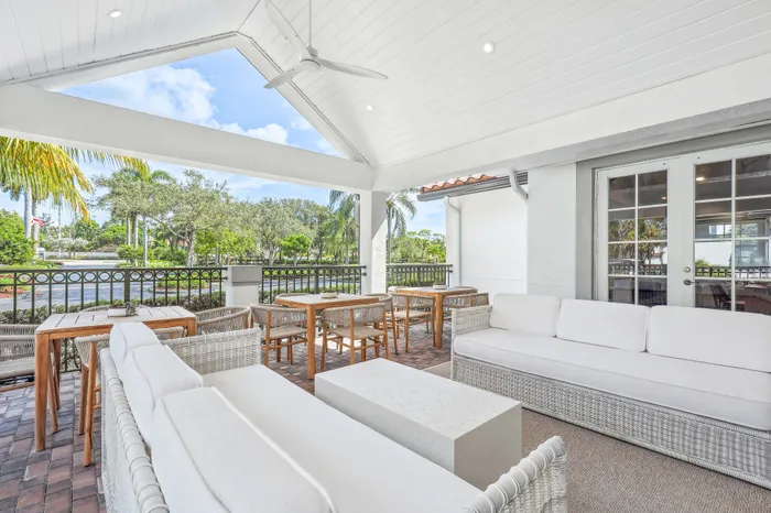 Chic outdoor patio with white wicker furniture, modern ceiling fan, and lush greenery, perfect for relaxing and entertaining.