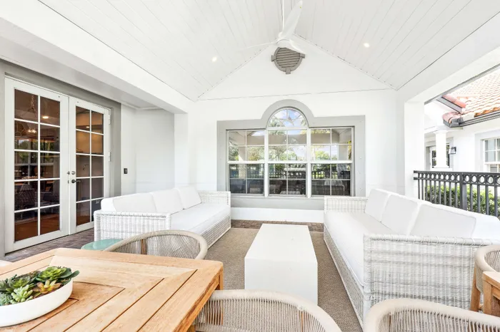 Chic covered patio with white wicker sofas, wooden dining table, and lush outdoor views.