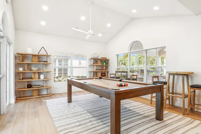 Bright and inviting recreation room featuring a stylish billiards table, modern shelving, and expansive windows offering lush garden views.