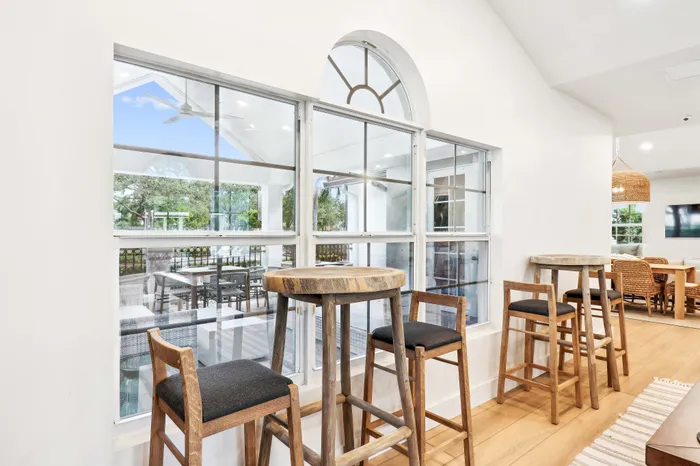 Modern apartment interior featuring stylish high tables with stools, large windows overlooking lush greenery, and a bright open concept layout.