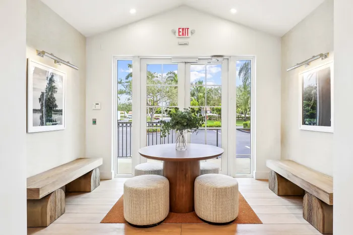 Chic apartment seating area with modern benches, round table, and lush greenery view through glass doors.