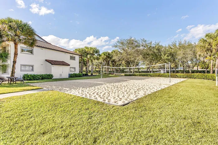 Inviting outdoor area with a sand volleyball court adjacent to a charming residential building, surrounded by lush greenery and palm trees.