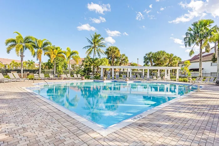 Luxurious outdoor pool area surrounded by palm trees and elegant sun loungers, perfect for relaxation under the clear blue sky.
