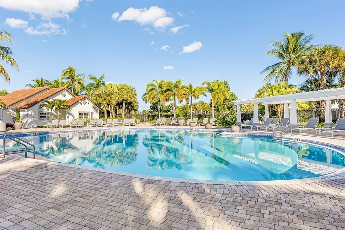 Exquisite outdoor pool area with pristine water, surrounded by lush palm trees and elegant lounge chairs, under a bright blue sky.