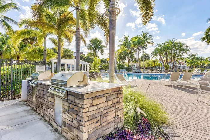 Inviting resort-style pool area featuring lush palm trees, elegant lounge chairs, and state-of-the-art outdoor barbecue grills.