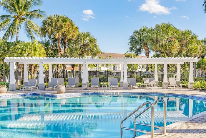 Inviting outdoor pool area with lush palm trees, elegant pergola, and relaxing lounge chairs for a resort-style experience.