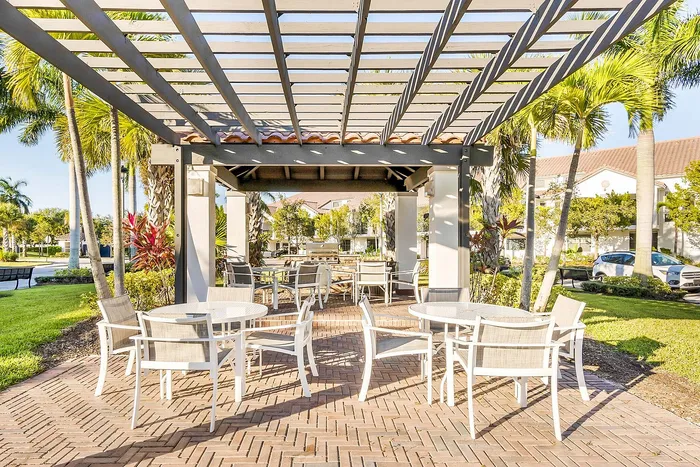Charming outdoor patio with elegant pergola and stylish seating surrounded by lush greenery and palm trees.